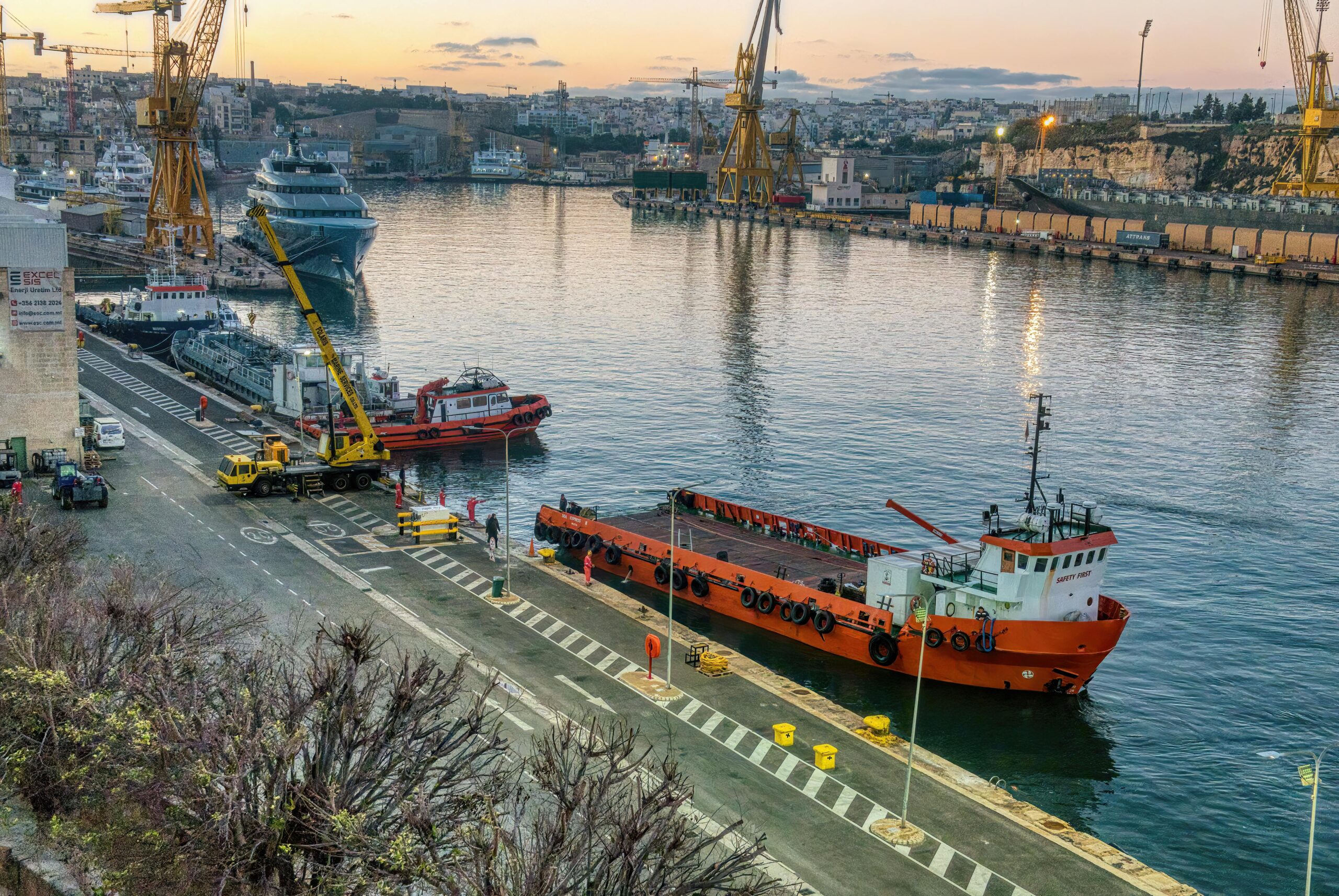 Vibrant sunset view of ships, cranes, and docks in a Maltese harbor.