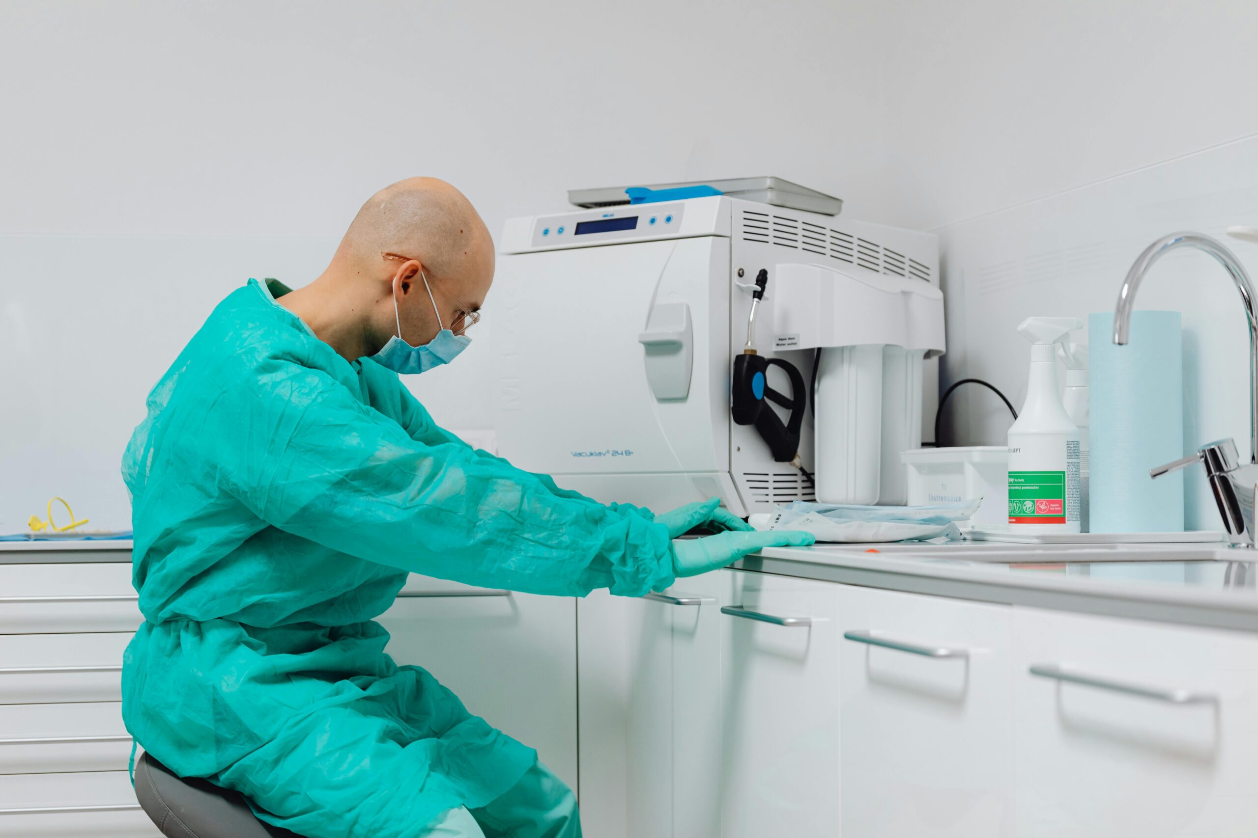 Dentist in sterile gloves and gown at dental office's cleaning area.