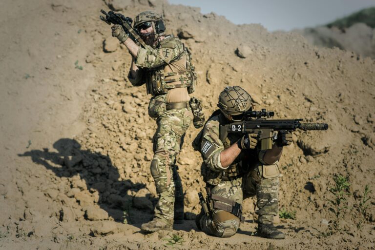 Two soldiers in camo engage in tactical training in a desert environment.